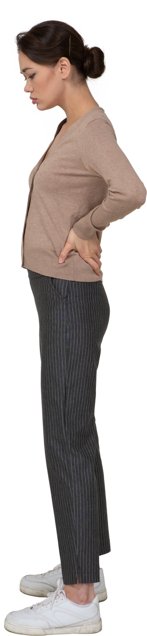 Vista laterale di una giovane donna in pullover e pantaloni, mettendo le mani sui fianchi e guardando in basso