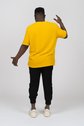 Rückansicht eines jungen dunkelhäutigen mannes in gelbem t-shirt, das die größe von etwas zeigt