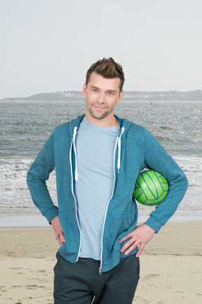 A man standing on a beach holding a green ball