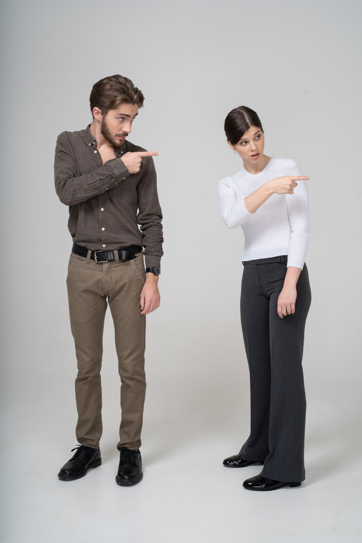 Front view of a young couple in office clothing pointing to the right
