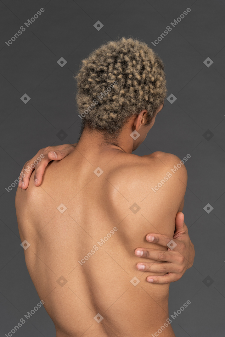 Vista posterior de un hombre afro sin camisa abrazándose a sí mismo