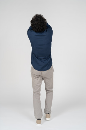 Rear view of a man in casual clothes covering face with hands