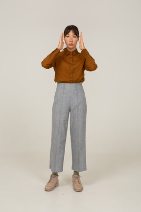 Vista frontal de una joven mujer asiática en calzones y blusa levantando las manos