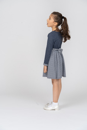 Three-quarter back view of a girl standing straight and looking dramatically to the side
