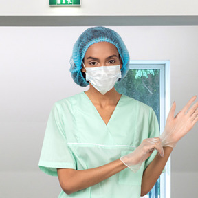 Enfermera en mascarilla poniéndose guantes