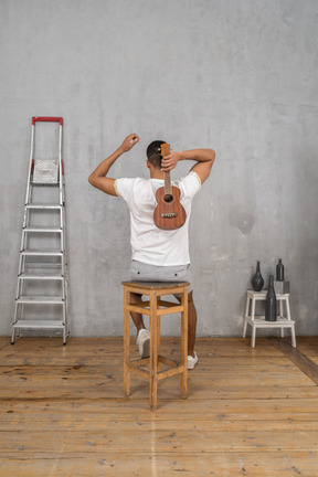 Back view of a man on a stool holding an ukulele behind his back