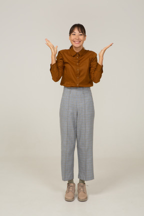 Vista frontale di una giovane donna asiatica felice in calzoni e camicetta che alza le mani