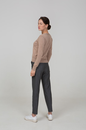 Vista posteriore di tre quarti di una giovane donna in pullover e pantaloni in piedi con gli occhi chiusi