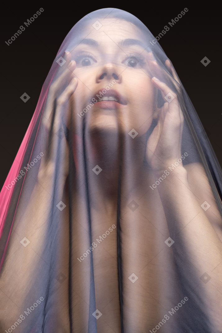 Front view of sensual naked young woman in dark veil looking with eyes widely open