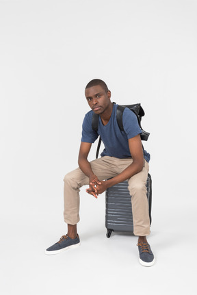 Pensive male tourist sitting on grey luggage