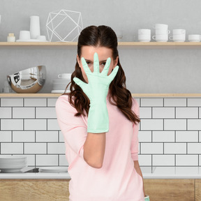 A woman in a pink shirt is covering her face with a green glove