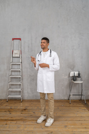 Vista frontal de un joven médico de pie en una habitación con escalera y silla que muestra el tamaño de algo