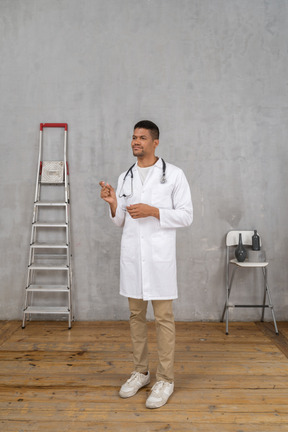 Front view of a young doctor standing in a room with ladder and chair showing a size of something