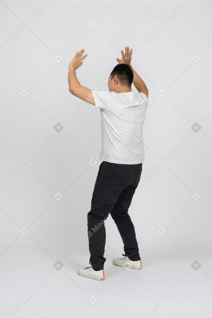 Rear view of a man in casual clothes standing with raised hands