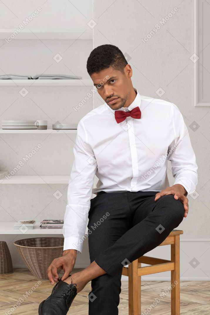 A handsome young guy sitting on a chair and touching his shoe