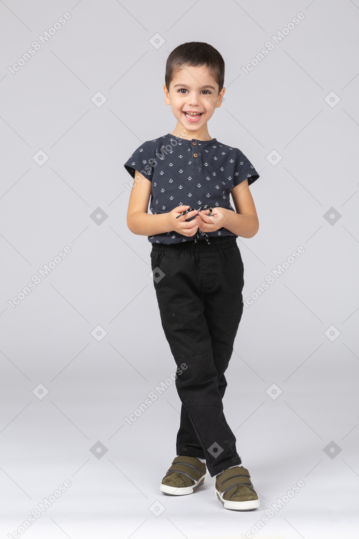 Front view of a happy boy standing with crossed legs and looking at camera