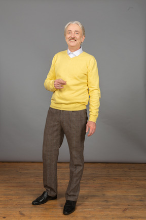 Vista frontal de um velho gesticulando vestindo uma blusa amarela e olhando para a câmera enquanto sorri