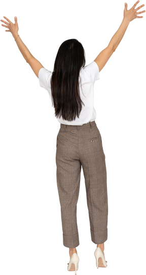 Vista traseira de uma jovem de calça e camiseta levantando as mãos