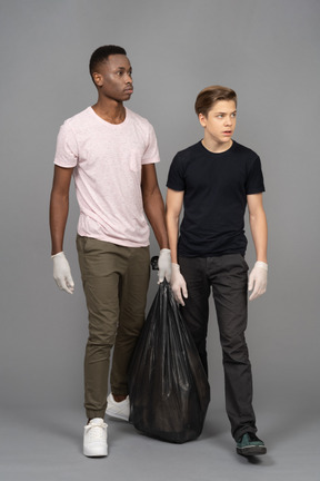 Two young man carrying a trash bag