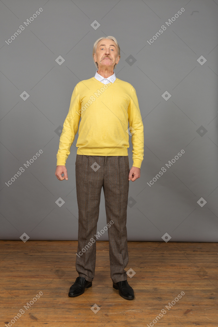 Vista frontal de un anciano curioso en jersey amarillo levantando la cabeza y mirando a la cámara