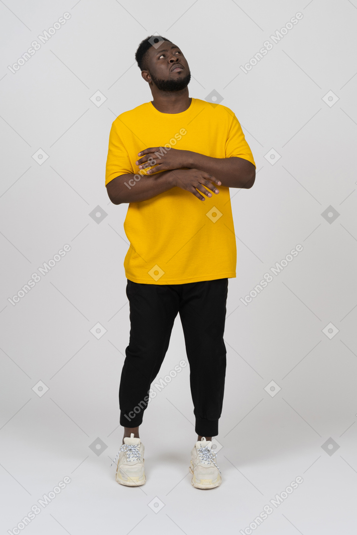 Vista frontal de um jovem de pele escura em uma camiseta amarela levantando as mãos