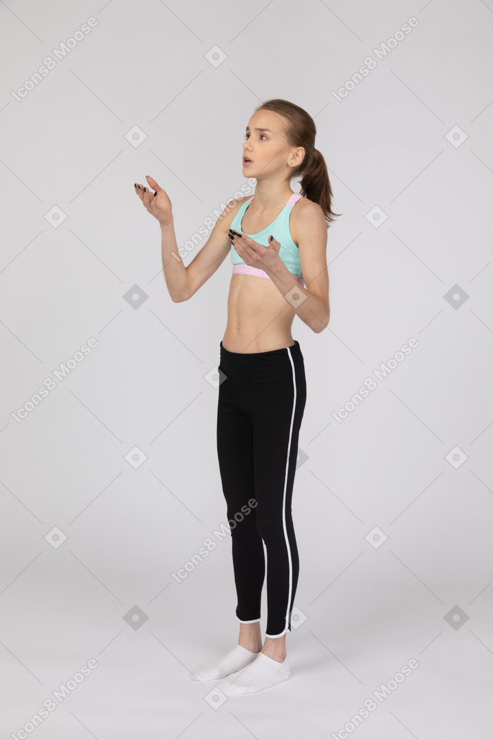 Вид в три четверти девушки-подростка в спортивной одежде, поднимающей руку и спорящей