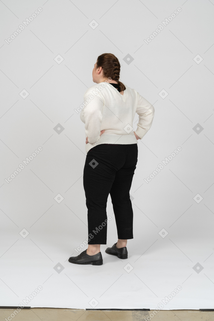 腰に手を置いて立っているカジュアルな服を着たふっくらとした女性の背面図