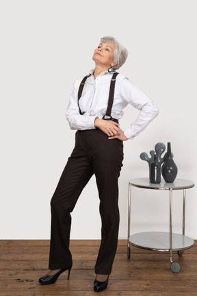 Вид в три четверти высокомерной старушки в офисной одежде, положившей руки на бедро