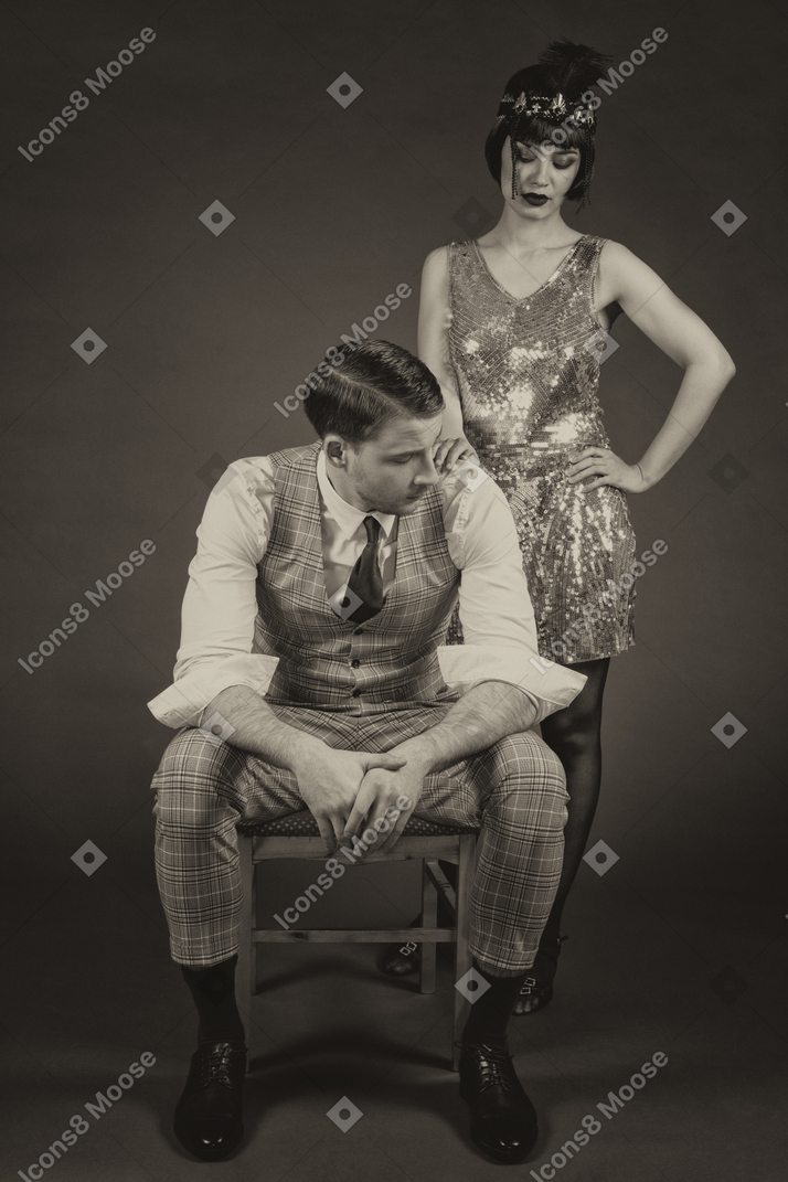 Elegante señorita de pie junto a un caballero bien vestido sentado en una silla
