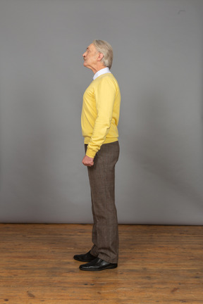 Vista laterale di un vecchio uomo curioso in pullover giallo alzando la testa e guardando da parte