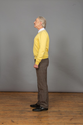 Side view of an old curious man in yellow pullover raising head and looking aside