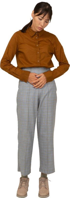 Vista frontal de uma jovem mulher asiática de calça e blusa, tocando o estômago