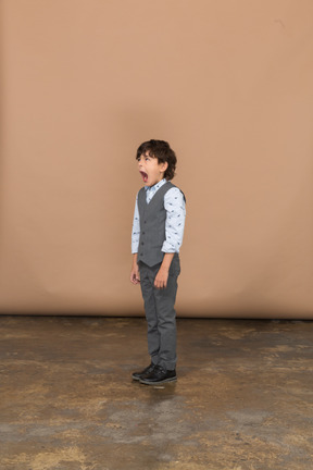 Vista laterale di un ragazzo vestito in piedi con la bocca aperta