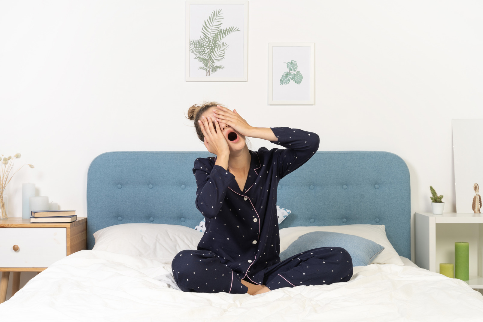 Front view of a yawning young woman in pajamas staying in bed and hiding face