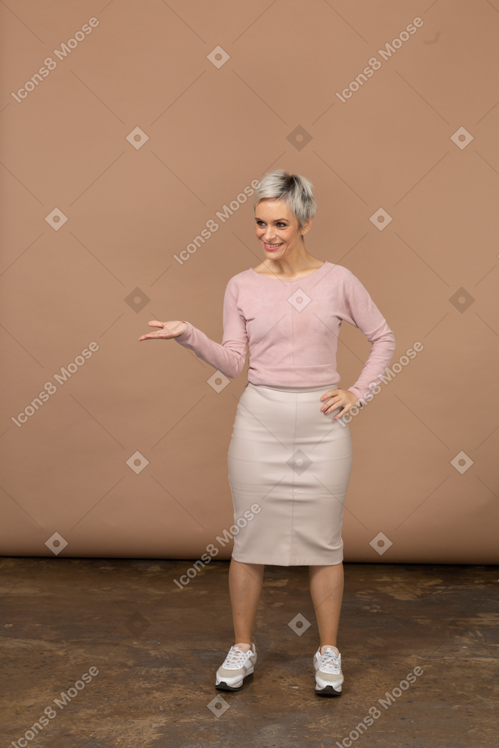 Vista frontal de uma mulher feliz em roupas casuais em pé com a mão estendida