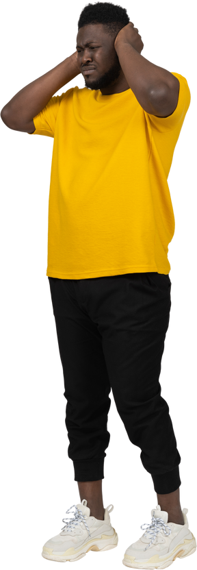 귀를 막고 있는 노란색 티셔츠를 입은 어두운 피부의 남자의 4분의 3 보기