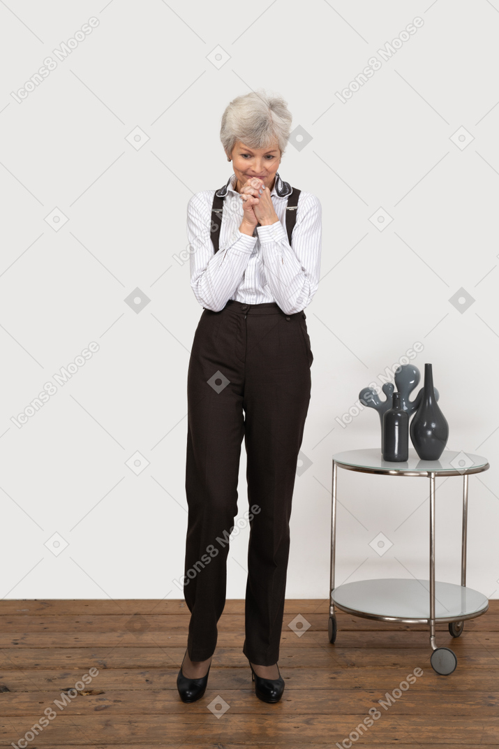 Front view of an intrigued old lady in office clothing holding hands near her face