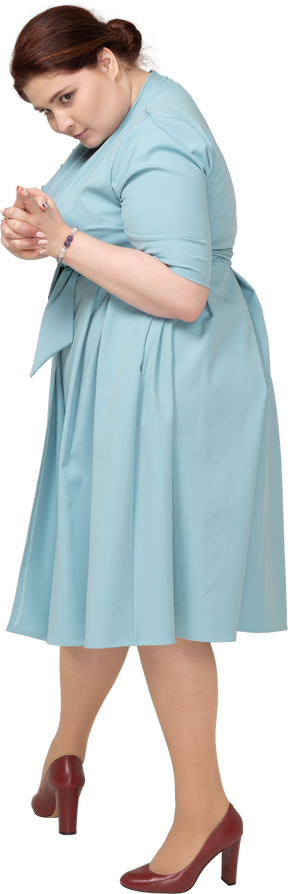 Вид сбоку женщины в синем платье показывает пистолет с пальцами