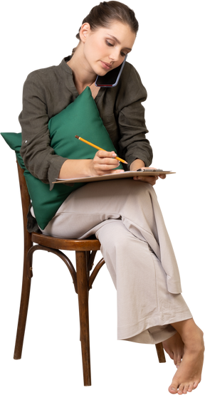 Front view of a young woman sitting on a chair with a tablet and having a phone call