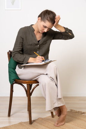 Вид спереди вдумчивой молодой женщины, сидящей на стуле во время прохождения бумажного теста