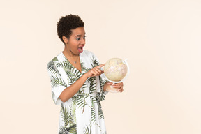 Femme aux cheveux courts noire vêtue d'une robe blanche et verte, debout avec un globe à la main