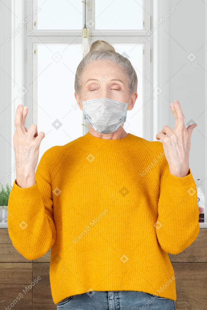 An older woman with face mask standing with fingers crossed