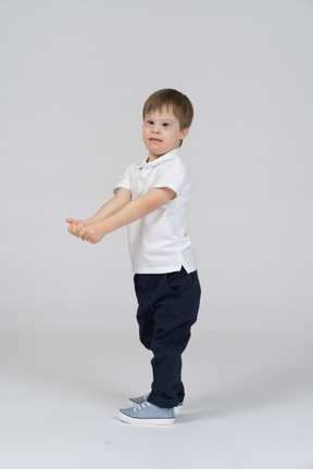 Side view of little boy standing with his hands extended forward