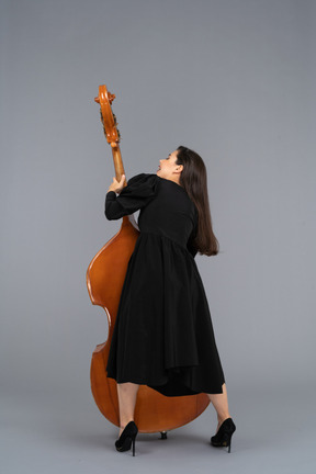 Back view of a young female musician in black dress holding her double-bass