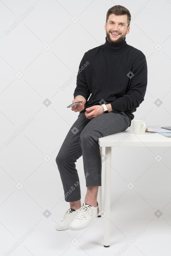 Entzückter geschäftsmann, der auf weißem schreibtisch sitzt
