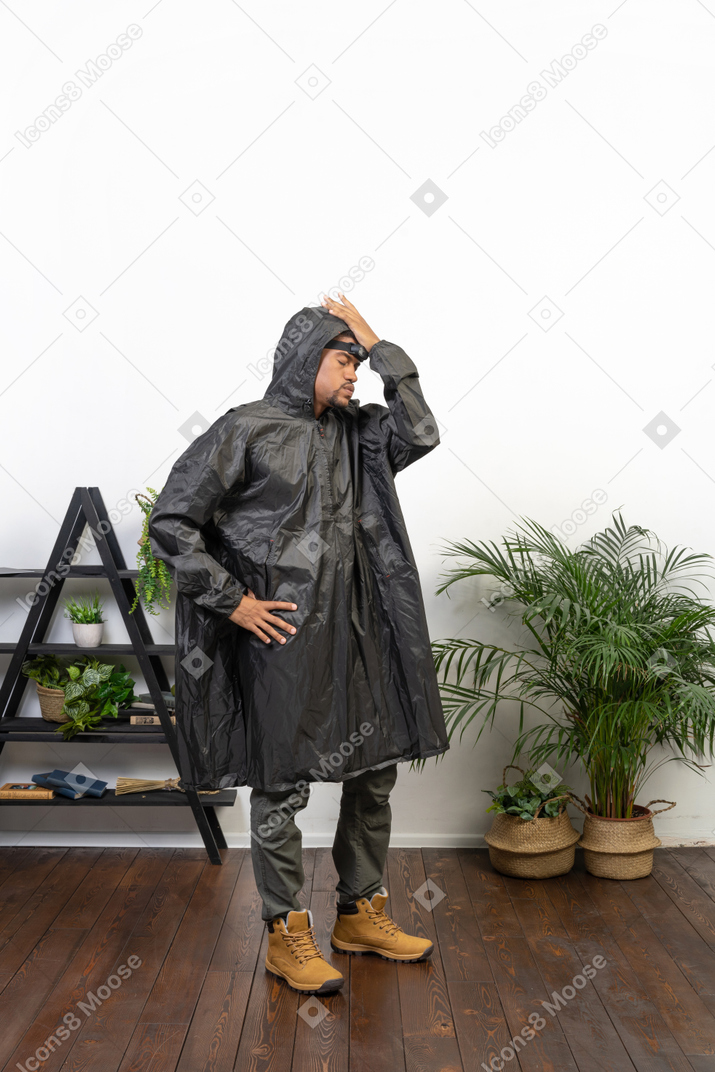 Homem cansado de capa de chuva em pé com a mão no quadril