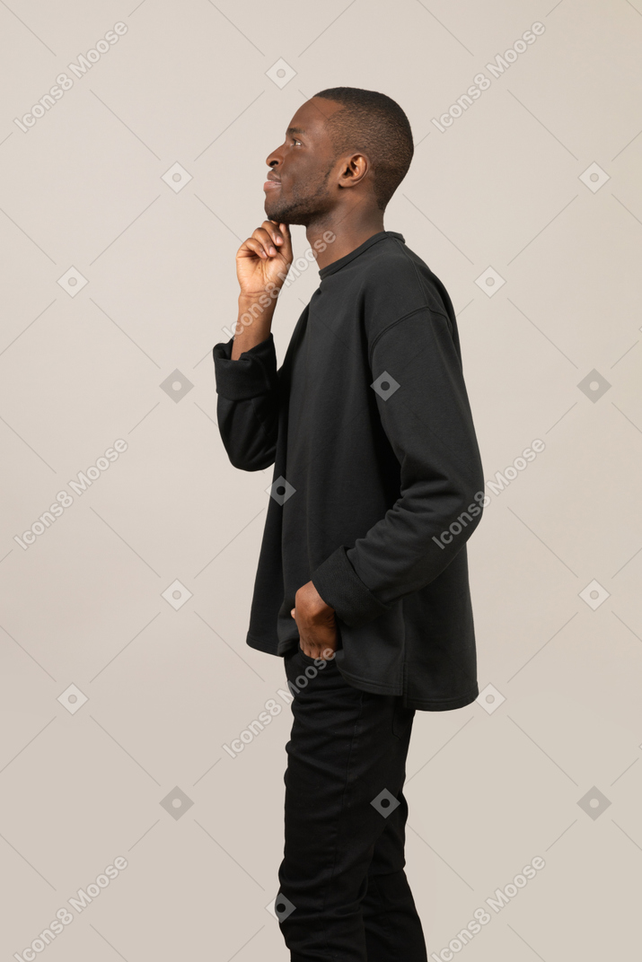 Side view of a young guy daydreaming with hand on chin