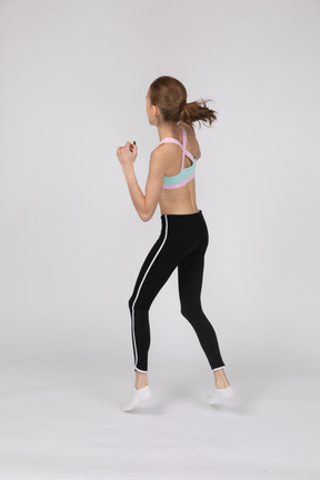 Back view of a teen girl in sportswear stepping forward while clenching fists