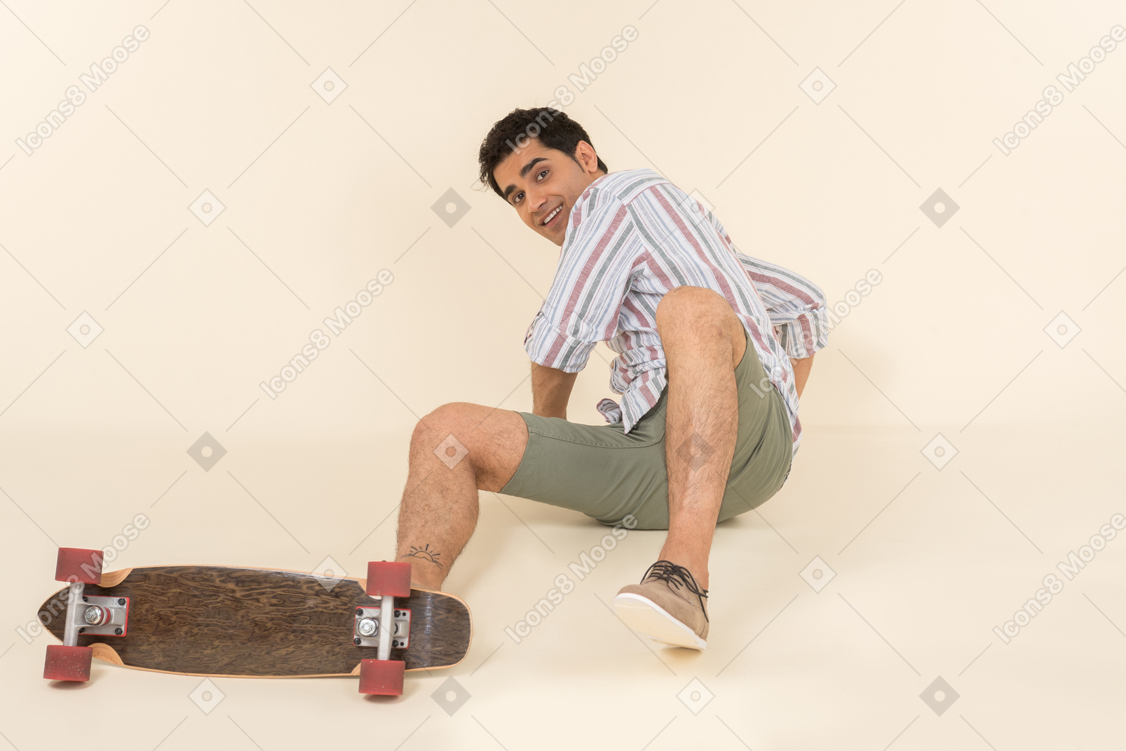A nice-looking caucasian guy in a striped t-shirt, having fun learning how to ride a skateboard