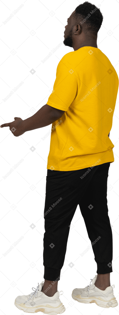 Vista traseira de três quartos de um jovem de pele escura em uma camiseta amarela apontando o dedo
